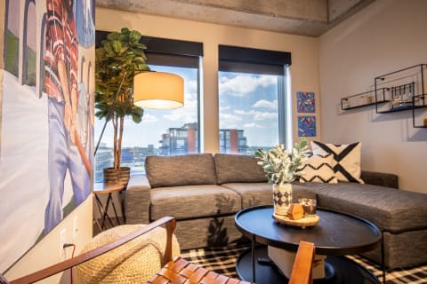 A stylish living room featuring a gray sectional sofa, wall mural, and large windows.