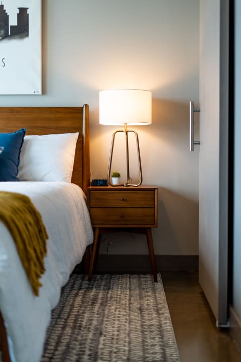 A modern bedroom featuring a wooden bed, a nightstand with a lamp and clock, and a decorative rug.