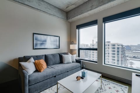 Contemporary living room featuring a gray couch, white coffee table, and large windows with city view.