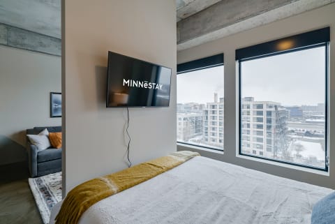 Interior of a modern bedroom featuring a bed, TV display, and city view.