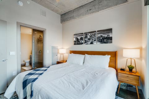 Modern bedroom with a bed, cityscape artwork, and warm lighting.