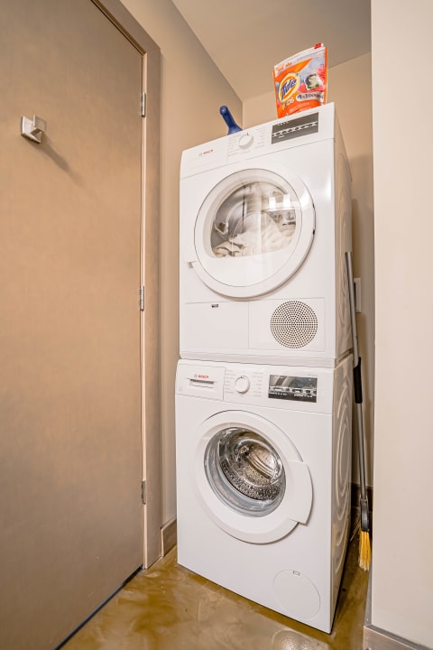 Laundry area with a stacked Bosch washer and dryer and a box of Tide detergent on top.