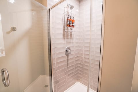 A contemporary shower enclosed by glass, featuring light tiles and a shower caddy with products.