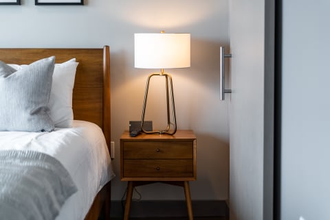 Modern bedroom corner with wooden bed, nightstand, and lamp.