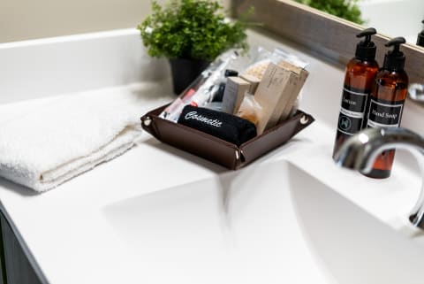 Bathroom sink with a folded towel, a tray of cosmetics, and amber pump bottles for lotion and hand soap.
