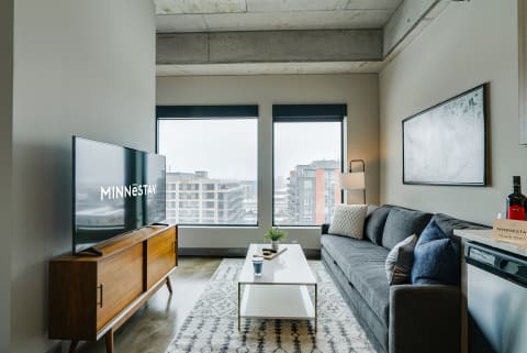 Modern living room featuring a gray sofa, a white coffee table, and large windows overlooking the city.