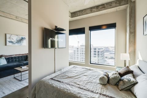 Stylish bedroom with a TV, decorative pillows, and a city view through large windows.