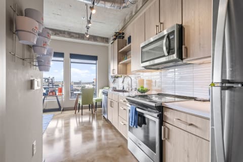 A sleek modern kitchen featuring light wood cabinetry and stainless steel appliances with a city view.
