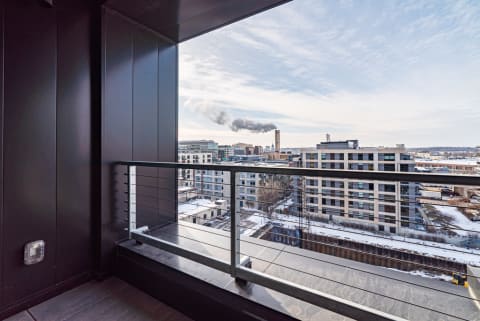 View from a contemporary balcony overlooking a snowy urban area with buildings and a smoke plume.