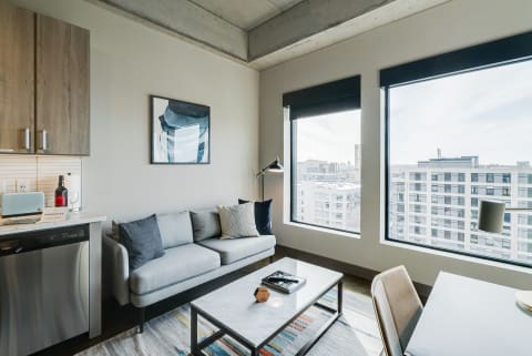 Modern living space with gray couch, artwork, and large windows showing city skyline.
