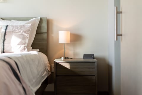 A cozy modern bedroom with a bed and nightstand featuring a lamp and speaker.