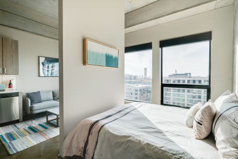 Modern studio apartment featuring a bedroom, kitchenette, and city skyline views.