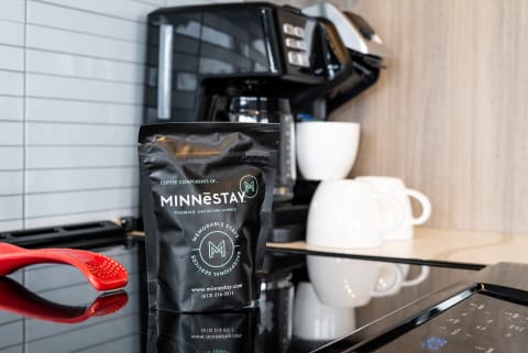 A coffee bag from MINNESTAY in a modern kitchen with a coffee maker and white mugs.