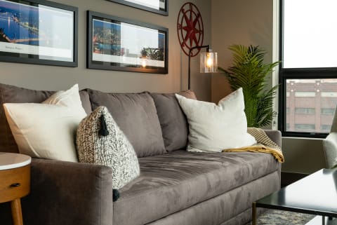 Cozy living room with a gray sofa, cushions, side table, and framed artwork.