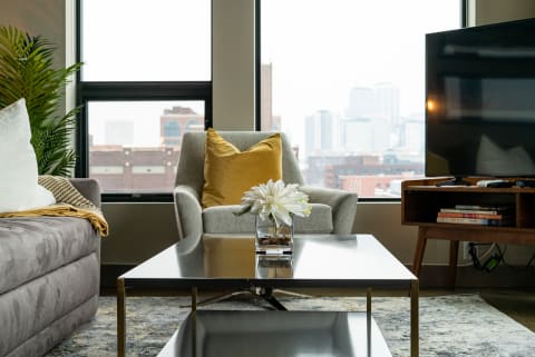 Cozy living room featuring a gray sofa, armchair, decorative coffee table, and city view through large windows.