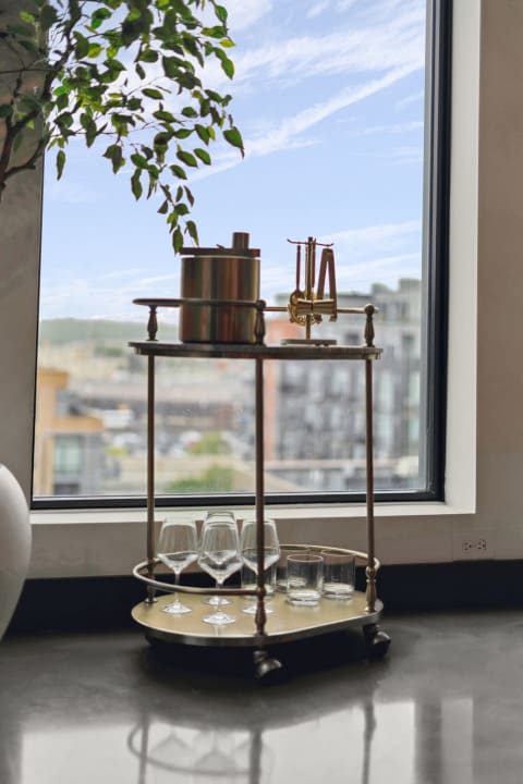 A drink cart with glassware and an ice bucket positioned by a window overlooking a cityscape.