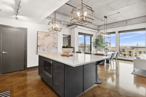 Open-concept kitchen and dining area featuring a marble island, modern light fixtures, and large windows.