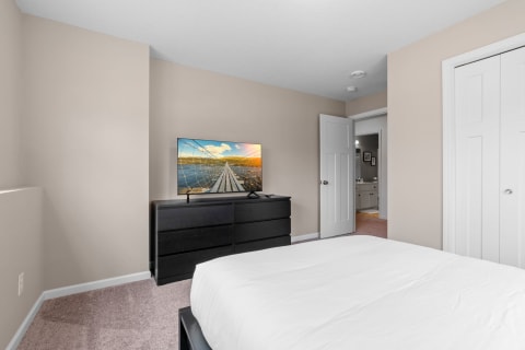 A cozy bedroom with a white bedspread, black dresser, and flat-screen TV showing a landscape image.