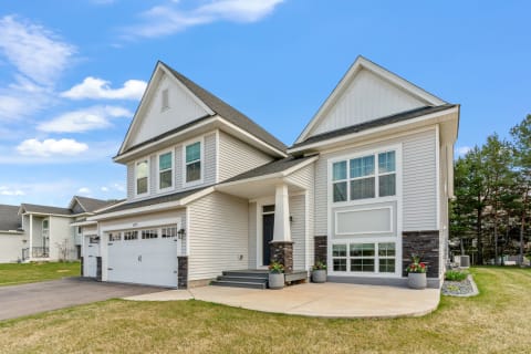 Two-story house with large windows and stone accents, featuring a welcoming porch and double garage.