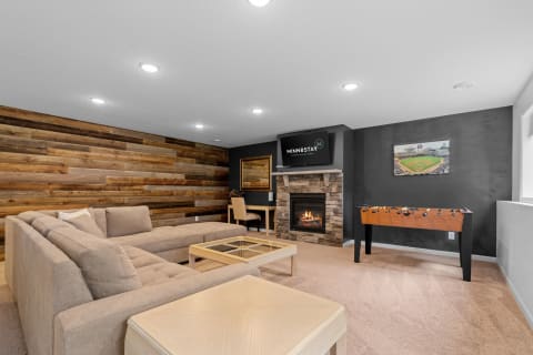Cozy basement living area featuring a sectional sofa, a fireplace, and a foosball table.