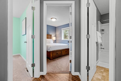 View of a hallway with a mint green wall on the left, a bathroom on the right, and a cozy bedroom in the background.