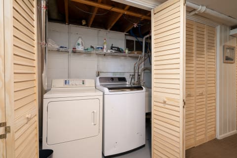 A clean laundry room with a washing machine, dryer, and shelves for laundry supplies.
