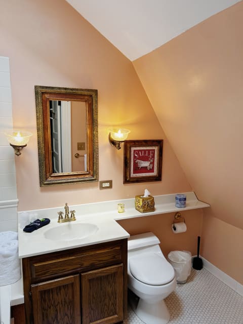 A cozy bathroom featuring a sloped ceiling, wooden vanity, and elegant fixtures.