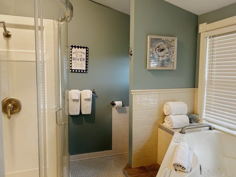 A cozy bathroom featuring a standing shower, plush towels, and a floral artwork on the wall.
