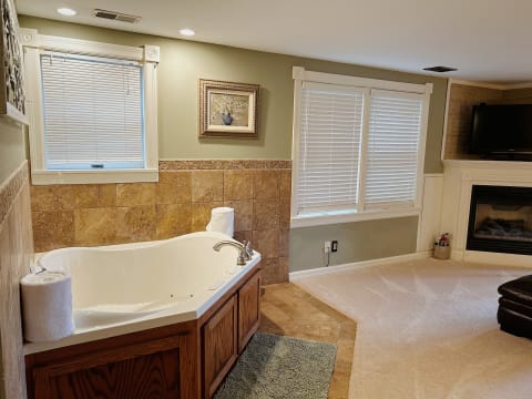 A luxurious bathroom featuring a jetted tub, a fireplace, and elegant travertine accents.