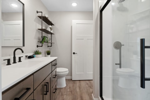 A contemporary bathroom with a white countertop, dark wooden cabinets, and a glass shower enclosure.