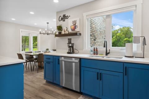 Modern kitchen with blue cabinets, stainless steel appliances, and a view of greenery outside.