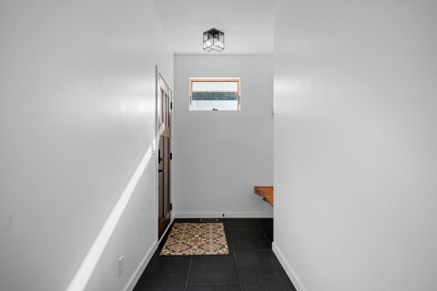 Minimalist hallway with white walls, wooden door, and dark tile floor.
