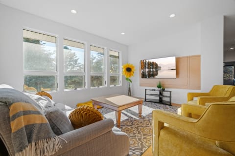 Bright living room with large windows, grey sofa, yellow armchairs, and a sunflower decoration.