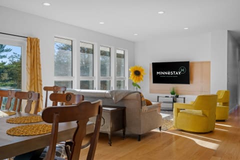 A modern living room with a dining table, yellow chairs, and a sunflower decoration next to a TV.