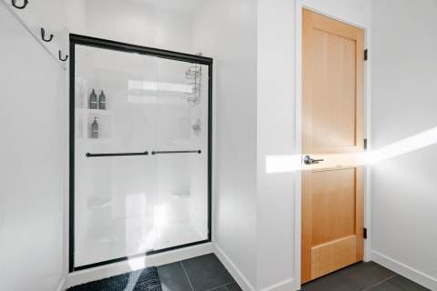 Contemporary bathroom corner with glass shower, shelves, and wooden door.