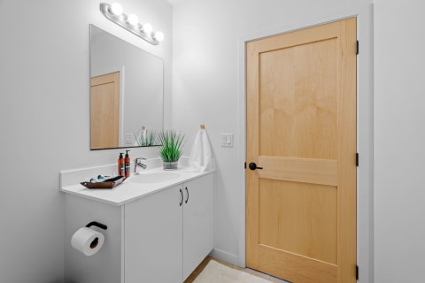 A bright, modern bathroom featuring a white countertop, large mirror, and wooden door.