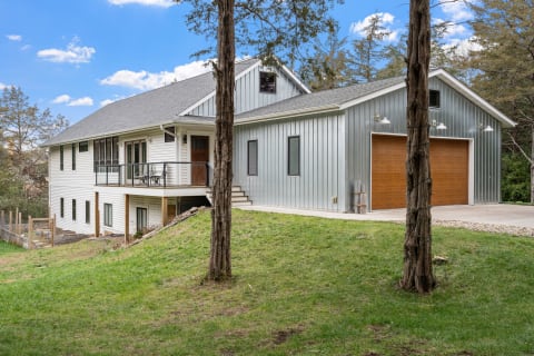 Two-story house with white and gray siding, featuring a front porch and garage, surrounded by green grass and trees.