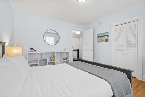 Cozy bedroom featuring a bed with white bedding, a grey blanket, and a modern bookshelf with books and a plant.