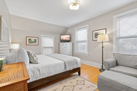 A cozy bedroom featuring a neatly made bed, gray sofa, and framed artwork.