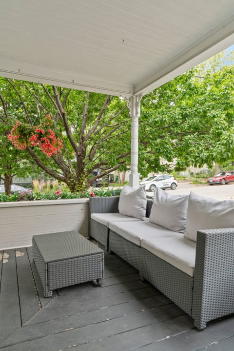 A stylish porch featuring gray wicker furniture and a view of greenery.