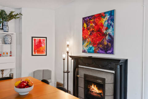 Dining area featuring a wooden table with fruits, a fireplace, and colorful artwork on the walls.