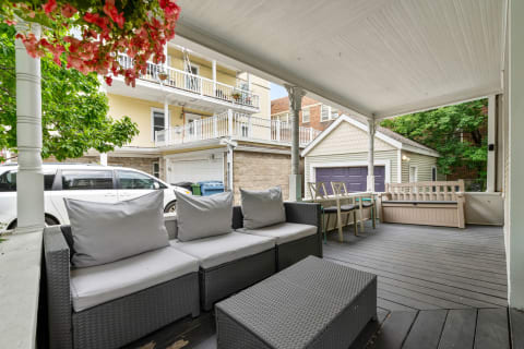 An inviting outdoor patio with gray cushions, wicker furniture, and pink flowers, overlooking residential buildings.