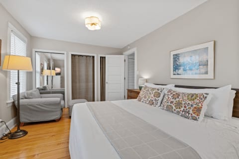 Cozy bedroom featuring a bed, colorful pillows, gray couch, and wooden flooring.