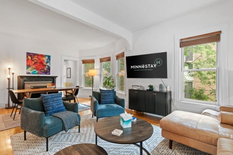 Cozy living room with teal chairs, a wooden table, and large windows.