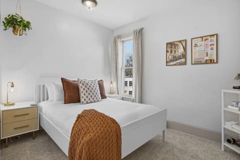 A cozy and bright bedroom featuring a white bed, earthy accents, and decorative artwork.