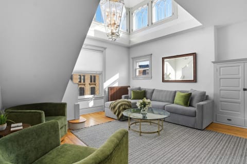 A stylish living room featuring a gray sofa, emerald green chairs, and plenty of natural light from the skylights.