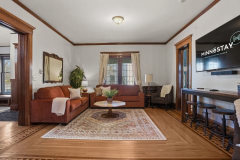 Elegant living room with rust-colored sofas, wooden accents, area rug, and modern bar seating.