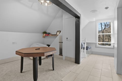 An upstairs room featuring a unique hexagonal game table and a relaxing seating area, bathed in natural light.