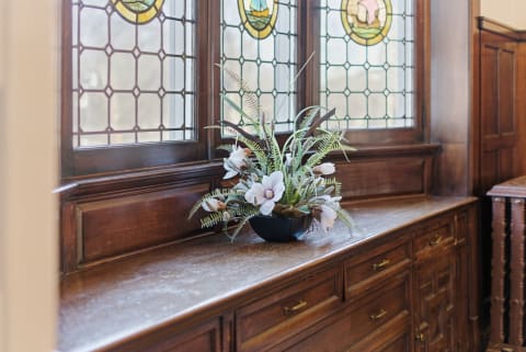 A floral arrangement in an elegant black vase on a wooden countertop beneath stained glass windows.