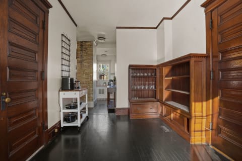 A butler's pantry with rich wood cabinetry, a cart with cookware, and a glassware-filled cabinet, all under soft lighting.